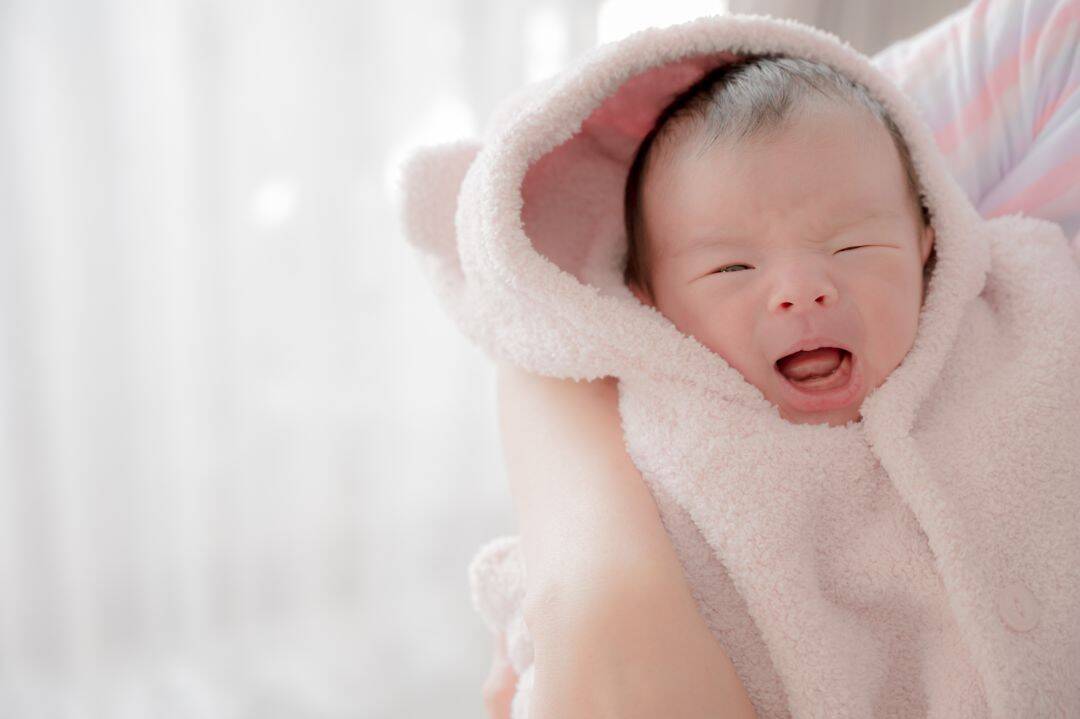Crying baby wrapped in a soft, pink blanket.