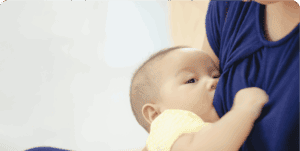Mother breastfeeding baby in yellow clothes.