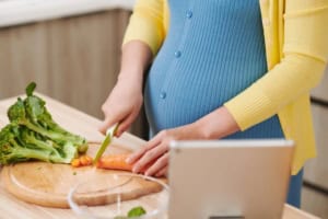 Pregnant woman chopping vegetables in kitchen.