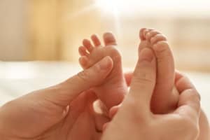 Hands holding baby's feet gently in sunlight