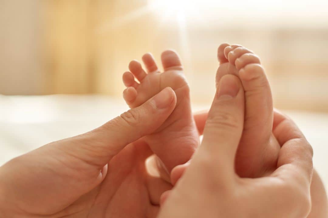 Hands holding baby's feet gently in sunlight