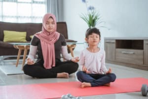 Mother and child meditating on yoga mat indoors.