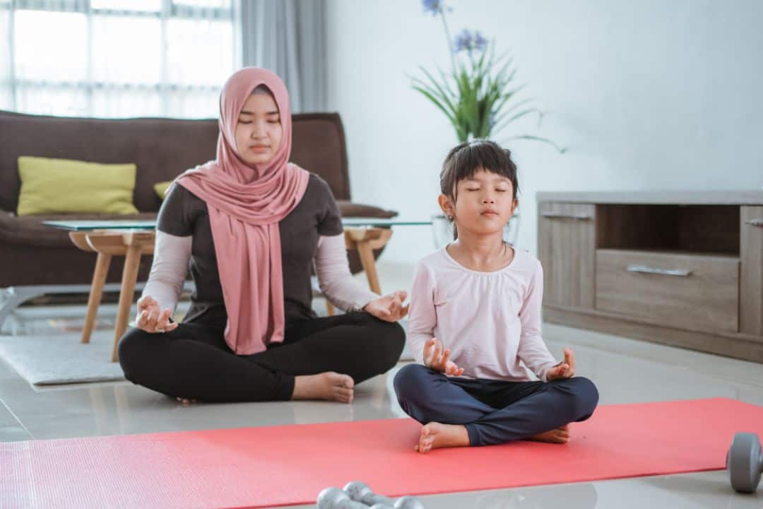 Mother and child meditating on yoga mat indoors.
