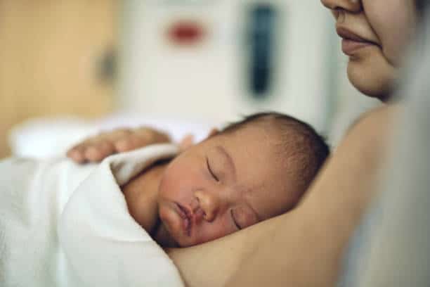 Baby sleeping on mother's shoulder, close-up of newborn care and maternal bonding.