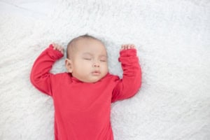 Sleeping baby in red outfit on white blanket.