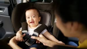 Smiling baby in car seat with caregiver.