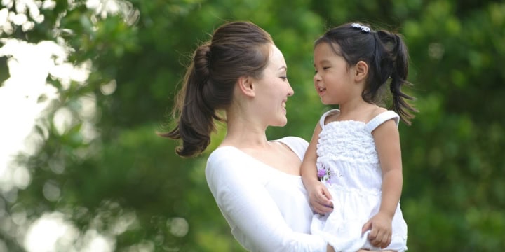 Smiling woman holding young girl in arms.